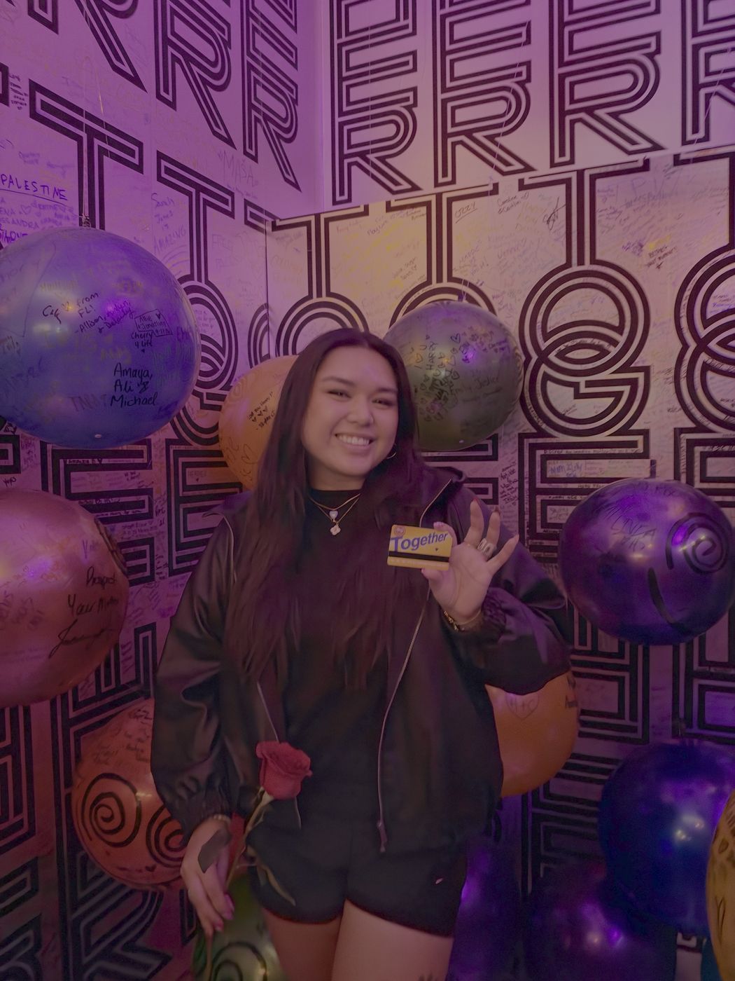 Carla smiling, holding a rose, in a room of purple balloons