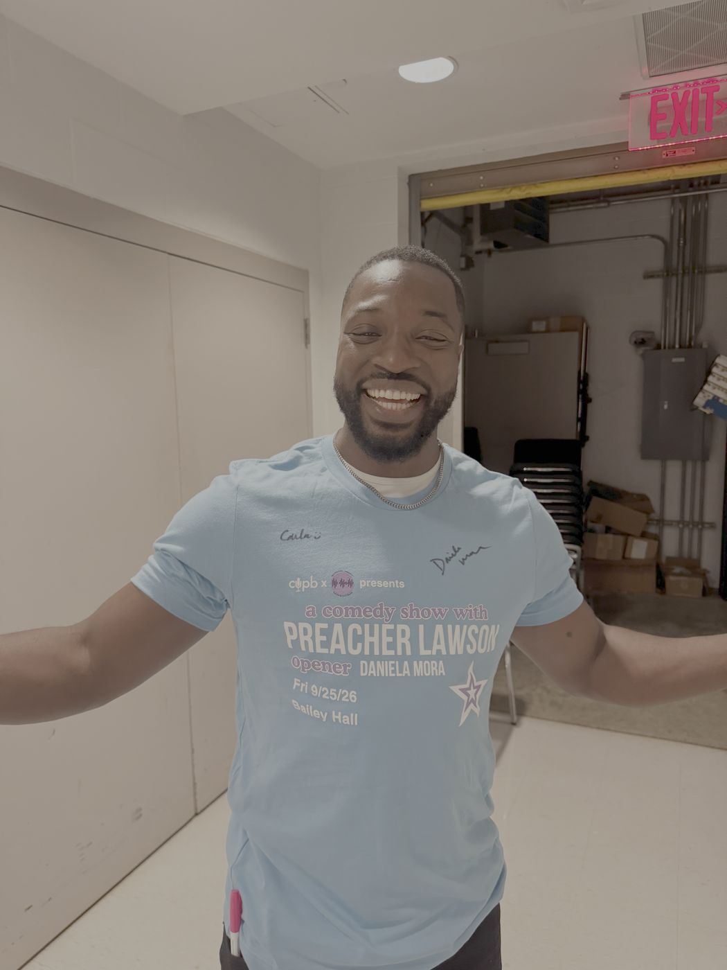 Preacher Lawson smiling backstage in a signed show tee